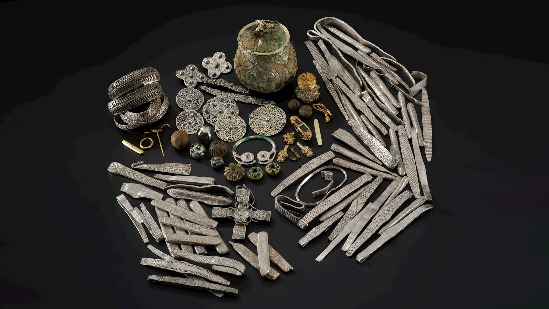 A hoard of (mainly silver) Viking treasure against a black backdrop.