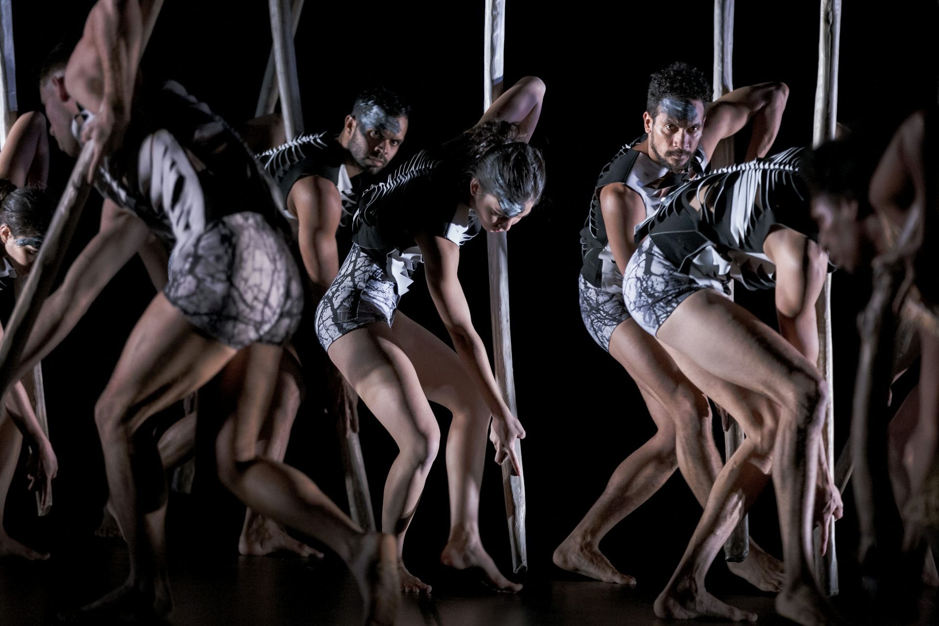 An ensemble of dancers in skeleton-like outfits march across a dark stage.