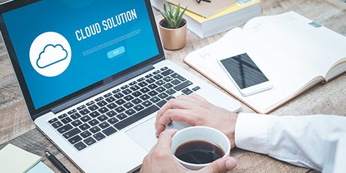 Laptop mit geöffneter Cloud-Solution-Seite, daneben Smartphone, Notizbuch und Kaffeetasse auf Schreibtisch