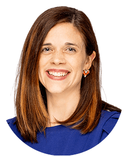 A woman with straight brown hair smiling, wearing a blue top and red earrings on a white background.
