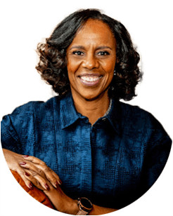 A person with shoulder-length curly hair smiles, wearing a dark blue textured top.