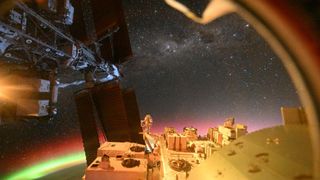 A view from the ISS that shows the ISS solar panels, auroras over Earth, and outer space with a vast array of stars.