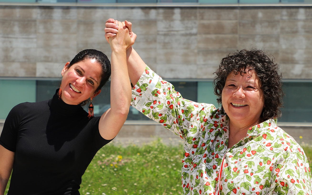 Two women standing outdoors, smiling, holding hands above their heads