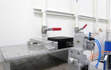 Một hình ảnh cận cảnh của một phòng thí nghiệm trưng bày một thiết bị cơ khí chính xác với hộp màu đen, kẹp kim loại và dây được kết nối trên nền trắng.