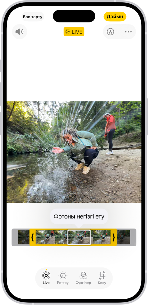«Фото» қолданбасында Live Photo ашық. Фотоның төменгі жағындағы — «Фотоны негізгі ету» түймесі белсенді кадрды қарау құралы. Кадрды қарау құралының екі жағындағылар — Live Photo суретін кесуіңізге мүмкіндік беретін екі көрсеткі. Экранның төменгі жағында: «Тікелей эфир», «Реттеу», «Сүзгілер» және «Кесу» түймелері. «Тікелей эфир» түймесі таңдалған.