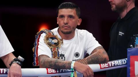 Lee Selby wears a white T-shirt with a Lonsdale belt over his shoulder, leaning on the ropes from the ring apron before a Joe Cordina fight in Cardiff