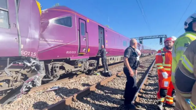 An image of a 360 train having crashed into an 810 train on a railway track, with emergency services nearby