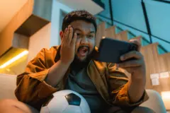 সোফায় শুয়ে স্মার্টফোনে সরাসরি ফুটবল ম্যাচ উপভোগ করছেন এক সমর্থক
