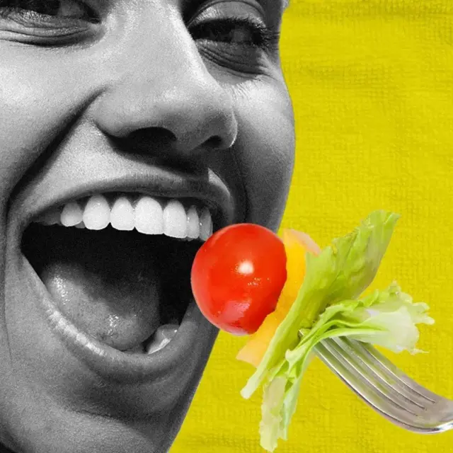 A woman in black and white looks into the camera while a forkful of tomato, pepper and lettuce heads towards her open mouth.