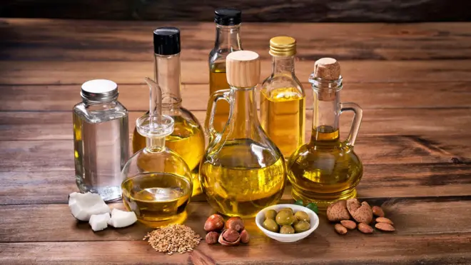 Assorted healthy vegetable oil bottle collection on wooden table in a old fashioned kitchen with low key illumination: Olive oil, hazelnut oil, almond oil, coconut oil and sesame oil
මුළුතැන්ගෙයක ලී මේසයක් මත තබා තිබෙන සෞඛ්ය සම්පන්න විවිධ වර්ගයේ එළවළු තෙල් බෝතල් එකතුවක්: ඔලිව් තෙල්, ලා දුඹුරු තෙල්, ආමන්ඩ් තෙල්, පොල්තෙල් සහ තල තෙල්.