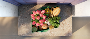 Vista aérea de la entrada de una casa con una bolsa de entrega de comestibles que contiene flores, pan, aceite de oliva y productos frescos, donde la forma de la bolsa forma el logotipo paralelogramo de Stripe.