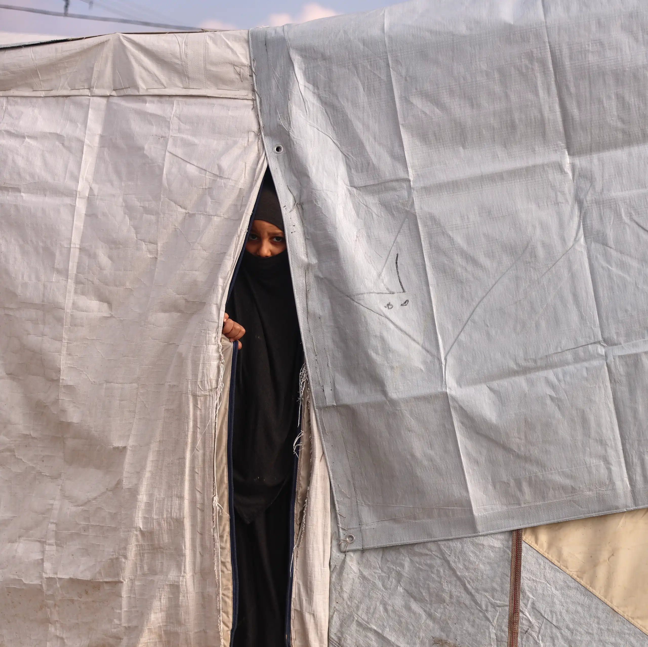 A woman in a niqab peers out of a white tent