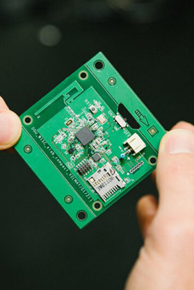 A green microchip is held in between two hands.