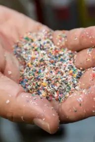 A hand holds colorful sand-like grains.