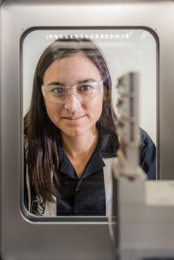 A scientist wearing protective eyewear looks into a lab chamber.