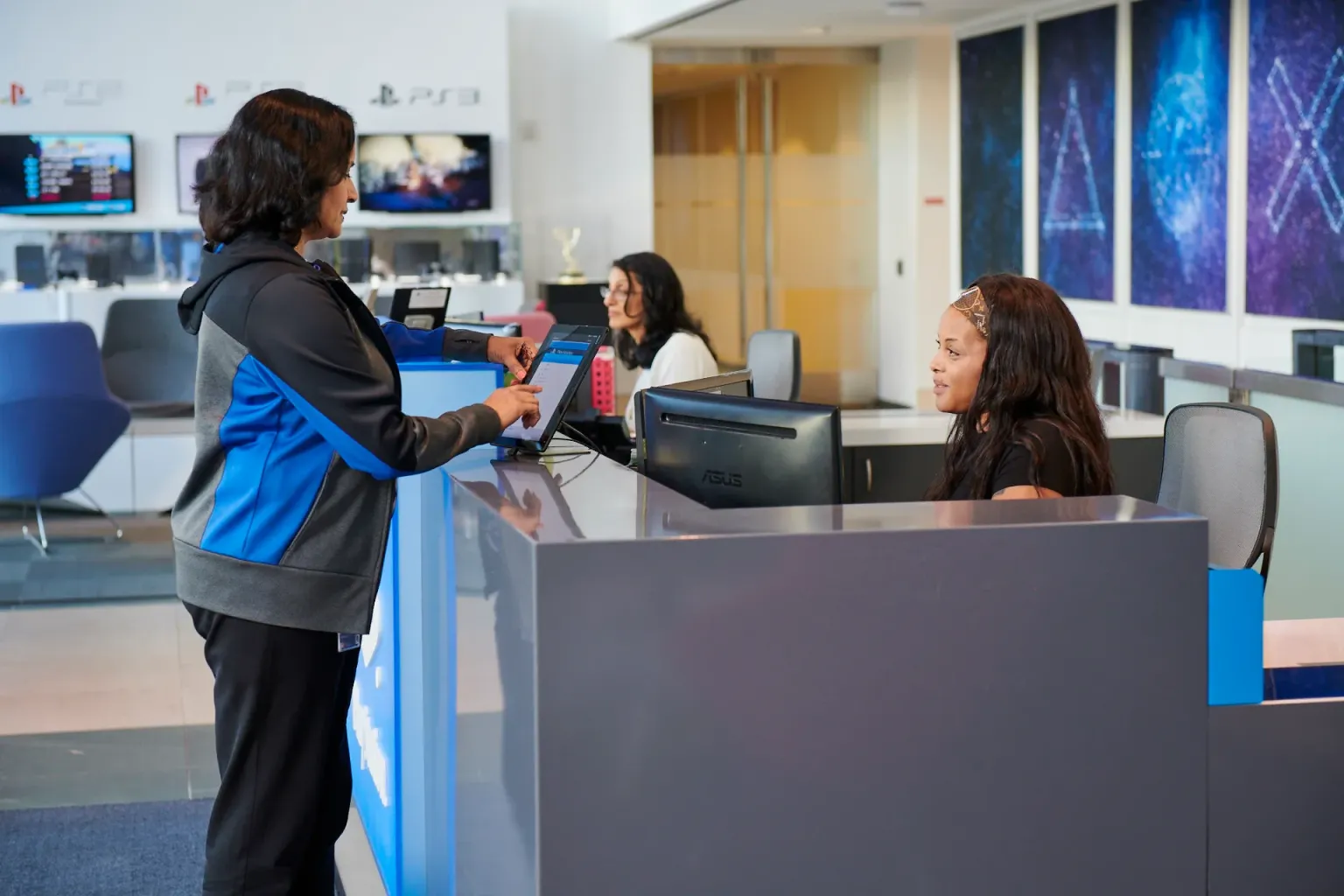 A woman in a gray and blue hoodie using a tablet at the PlayStation office reception desk.